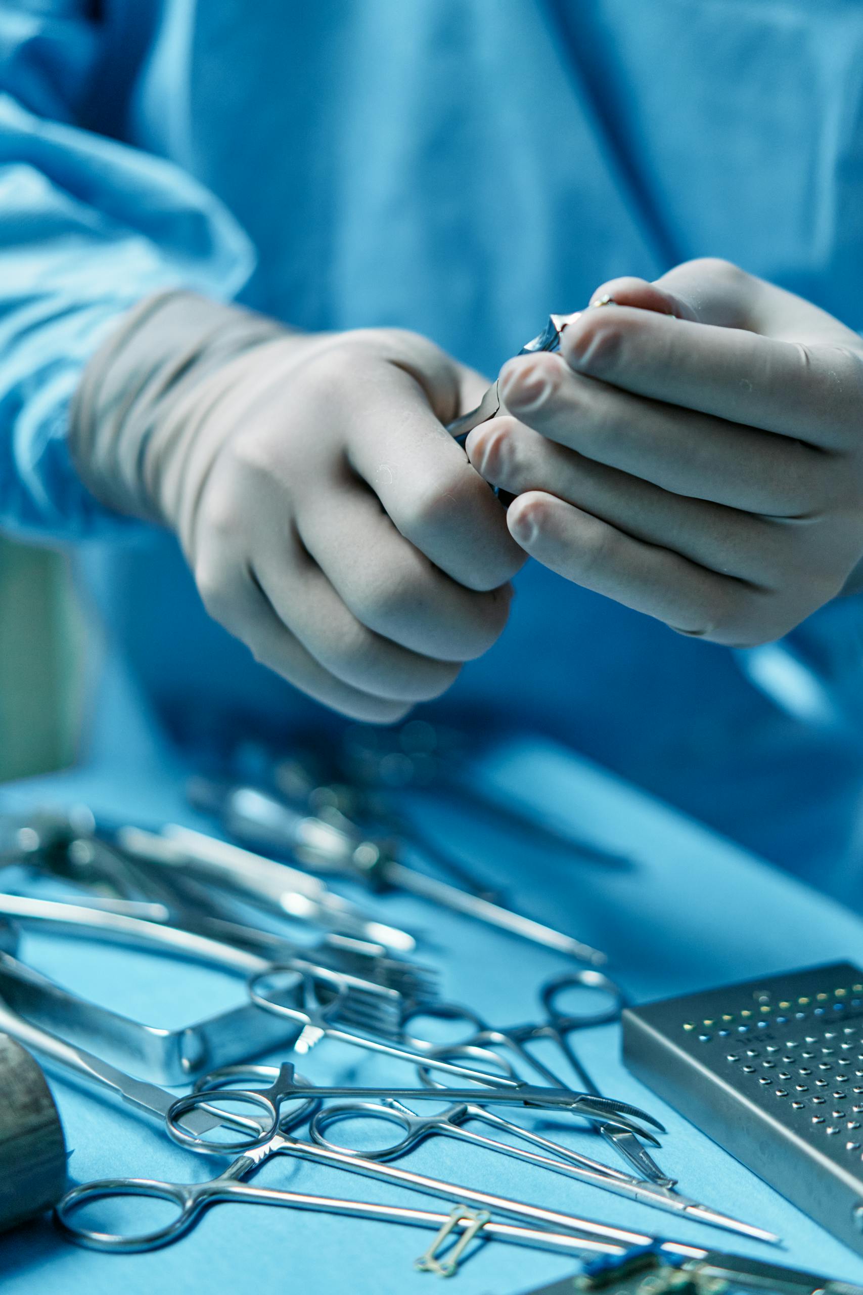 Close-up of surgeon's hands preparing tools for surgery in operating room.
